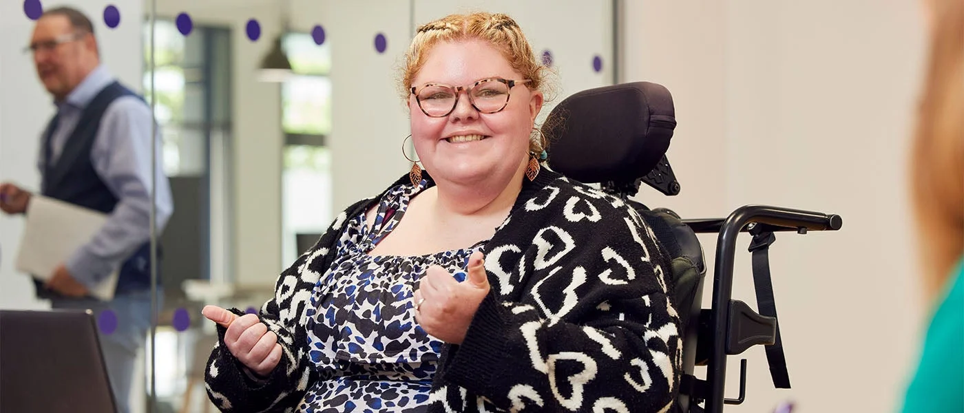 A disabled woman in a wheelchair smiling, giving a thumbs up